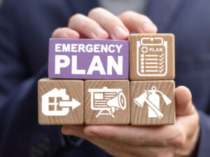 An image of someone holding blocks that say emergency plan, with images of a fire extinguisher, checklist, exit route and plan.